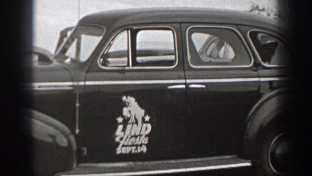 Black-and-white 1940 Washington home-movie frame showing a parked vintage sedan with Lind Fiesta Sept. 14 lettering on the door.
