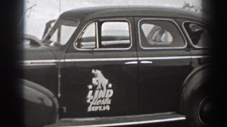 Black-and-white frame of a parked vintage sedan in Washington, with a visible Lind Fiesta Sept. 14 marking on the rear door.