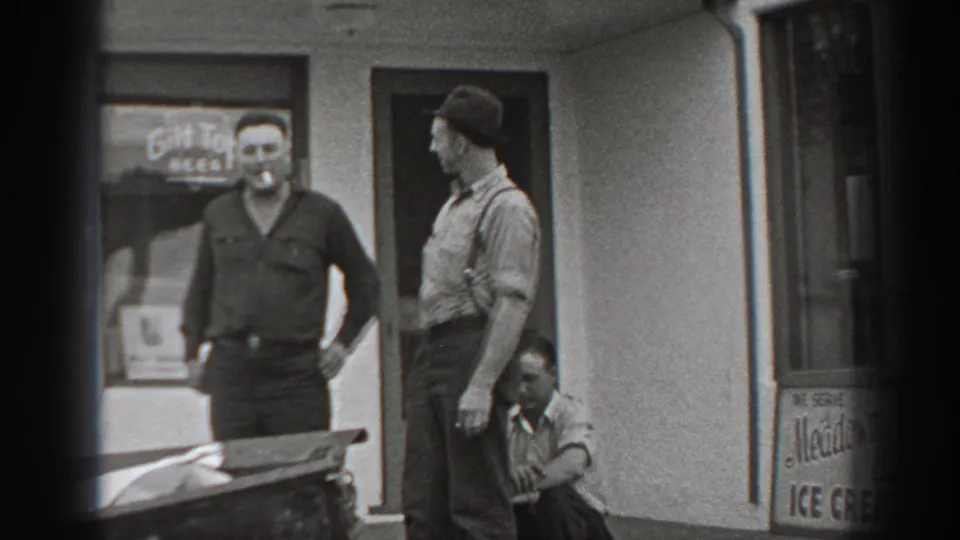Black-and-white Washington home-movie frame showing three adult men near a shop entrance and a visible beer sign in the window.