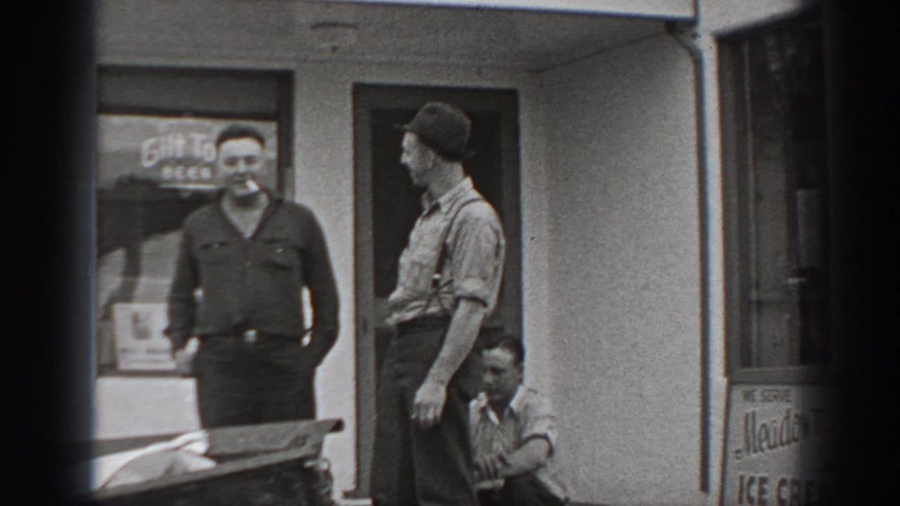 1940 Washington home-movie frame showing two standing men and one crouching man outside a storefront with beer signage.