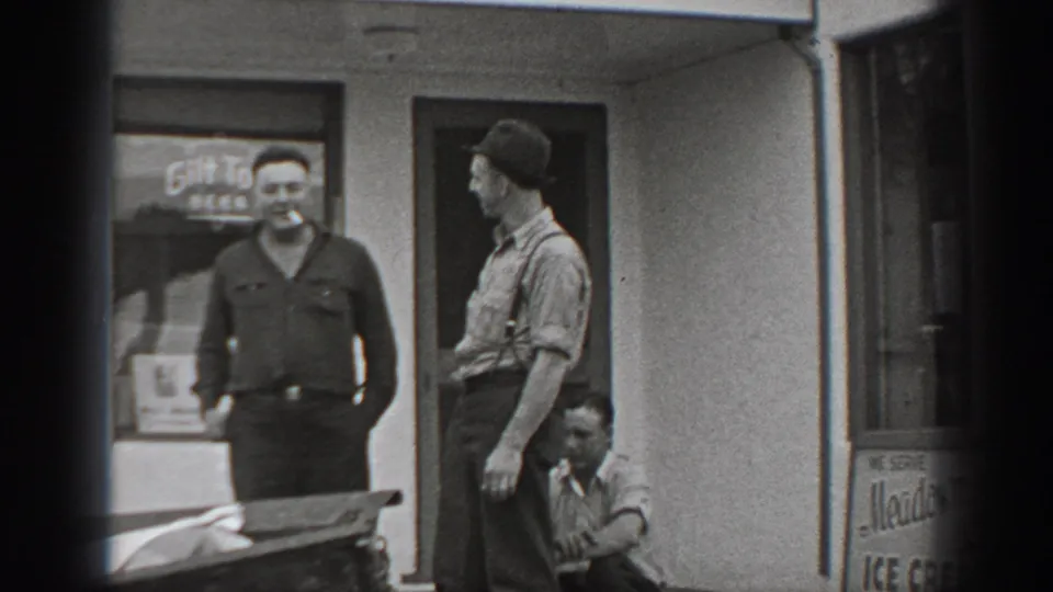 1940 Washington home-movie frame showing two standing men and one crouching man outside a storefront with beer signage.