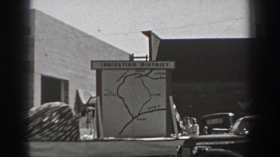 1940 Washington frame of an Irrigation District map board viewed from across the street with older cars nearby.