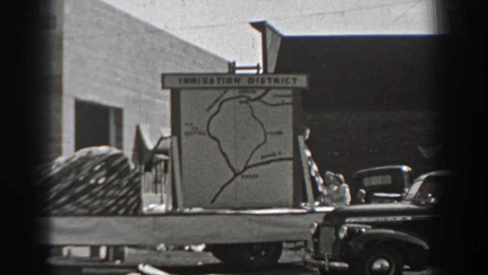 Final frame holds on the public irrigation district map, nearby trucks, coiled equipment, and small people at a sunlit Washington exterior location.