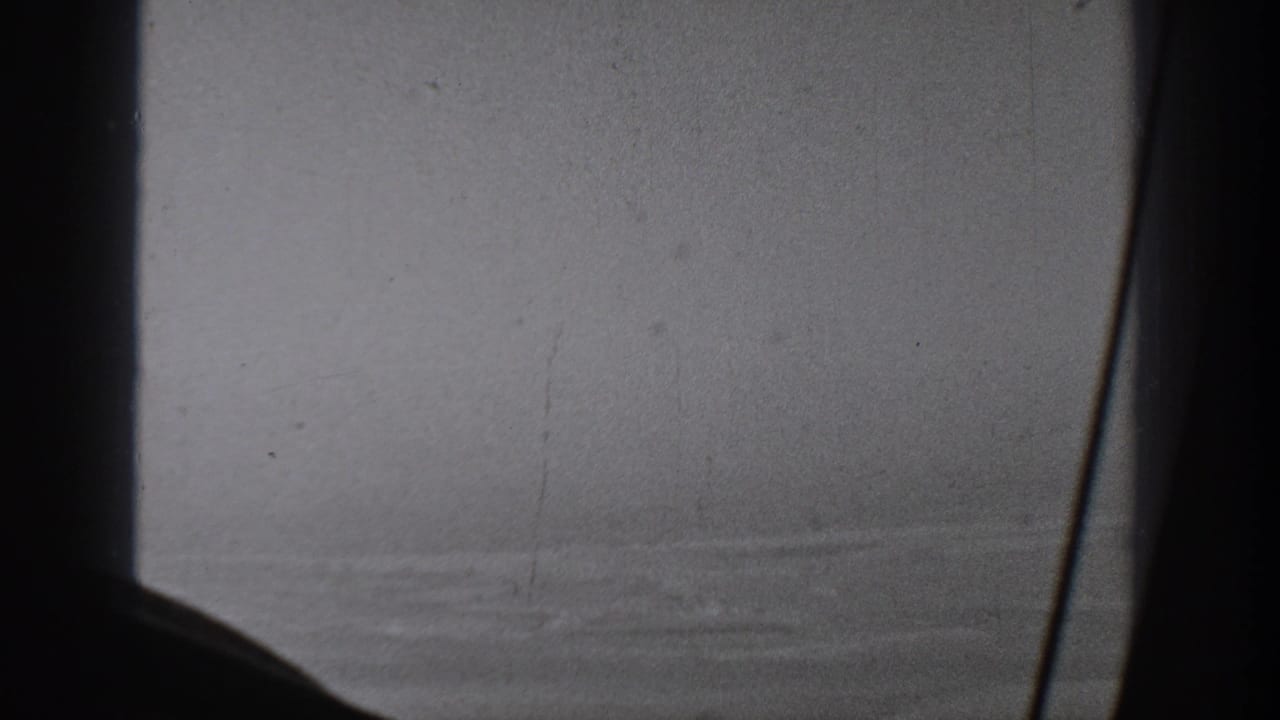 A dark window support cuts across a soft 1940s aerial view, with faint rural terrain visible through haze.