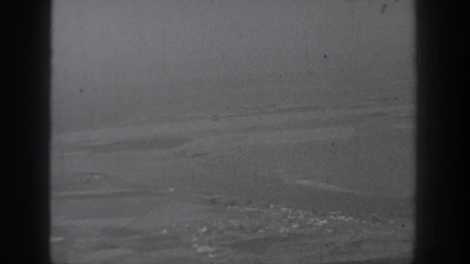 Aerial 8mm frame from Washington in 1940, showing patchy fields and a distant town area beyond a dark plane window bar.