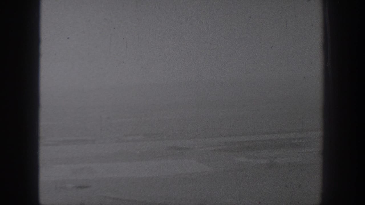 1940s Washington home-movie frame showing pale farmland from above with dark gate edges and soft monochrome texture.