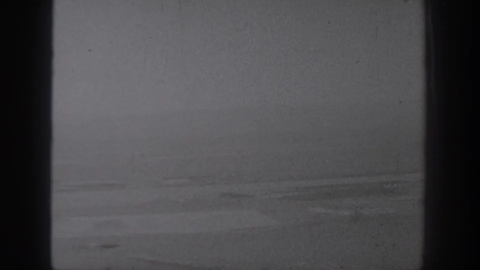 1940s Washington home-movie frame showing pale farmland from above with dark gate edges and soft monochrome texture.