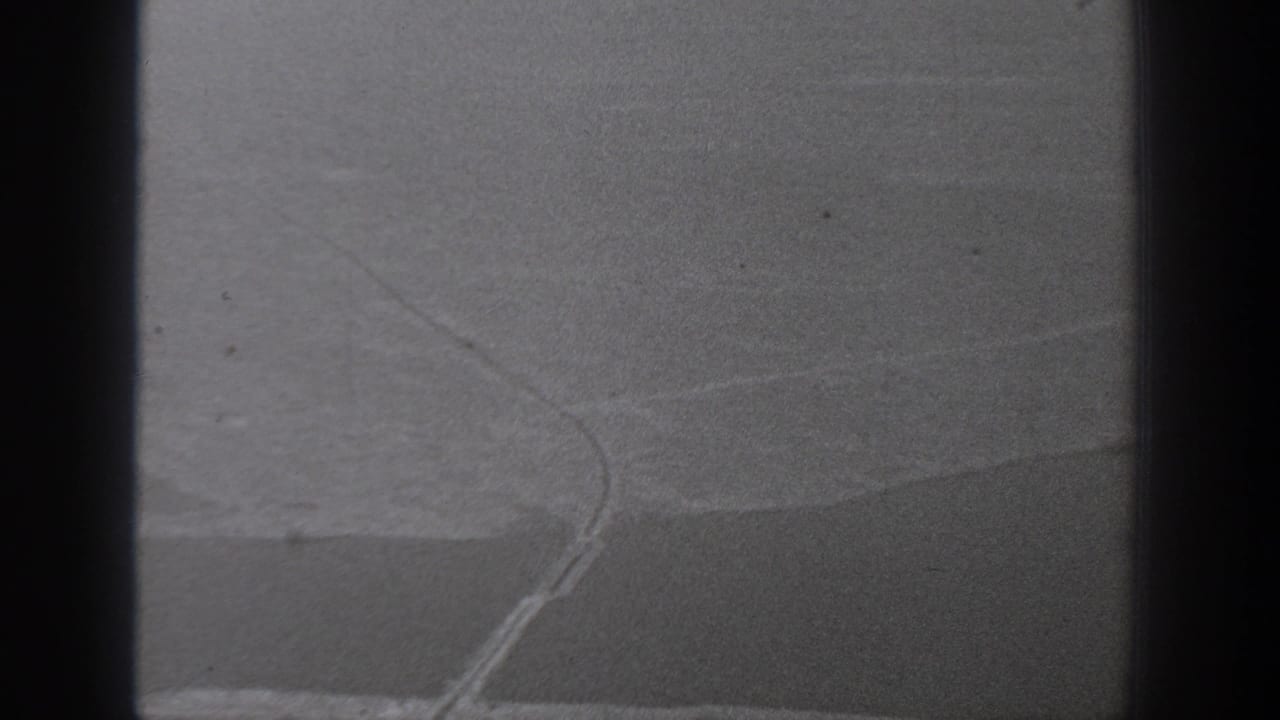 1940 Washington home-movie frame showing a soft, grainy view through dark bars toward a faint shoreline-like curve.
