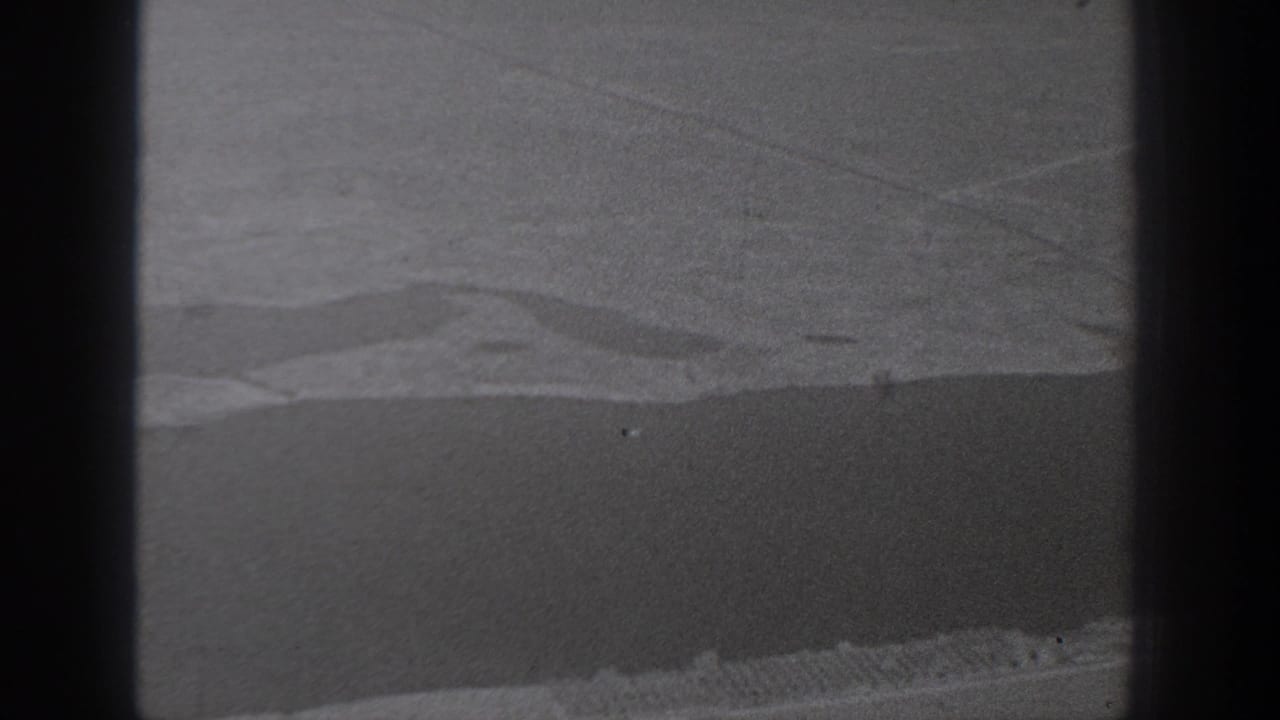 Dark center bar divides a grainy view of textured land or water with pale streaks near the top.