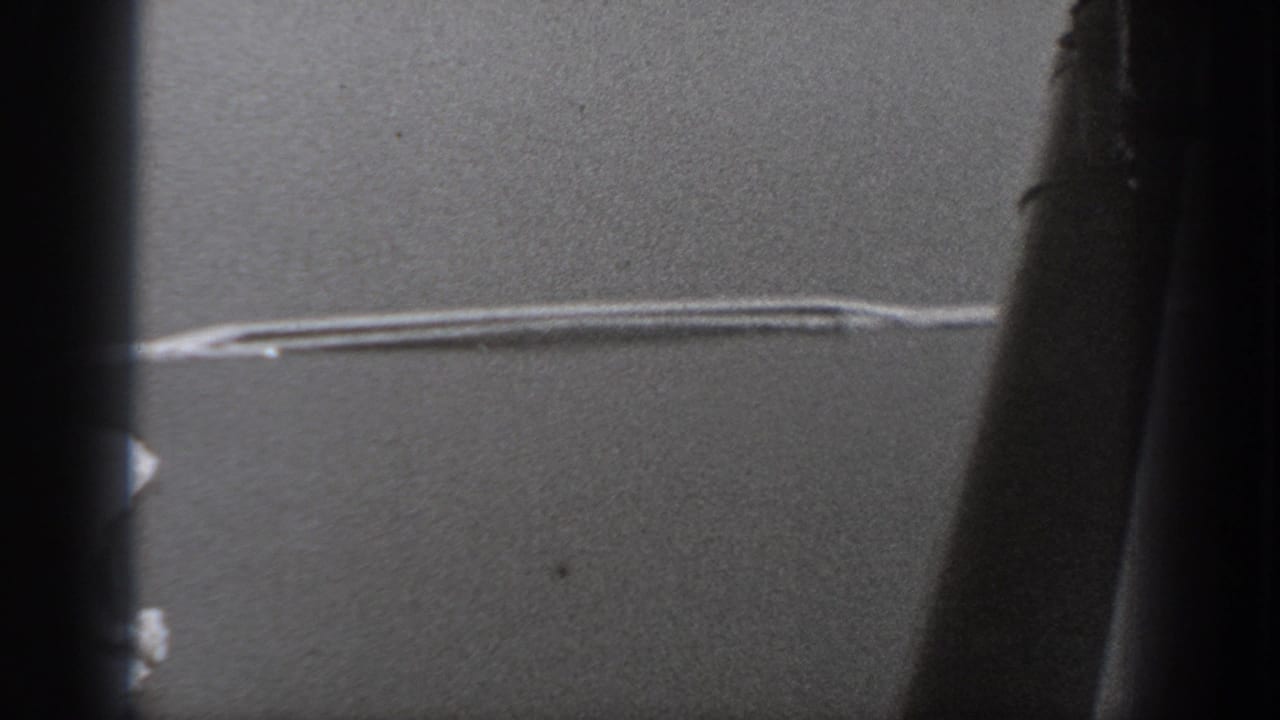 Aircraft-window view from the 1940 Washington home movie, showing dark framing and a pale linear mark across a gray exterior field.