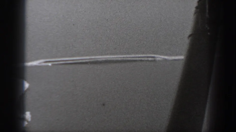 Aircraft-window view from the 1940 Washington home movie, showing dark framing and a pale linear mark across a gray exterior field.