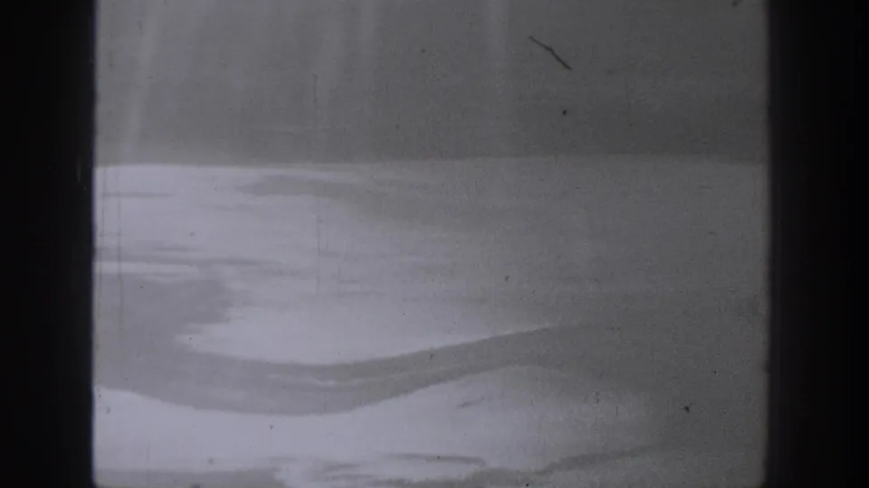 Late frame from the 1940 Washington clip showing a dark window edge and pale water-like shapes through grainy aircraft-window glass.