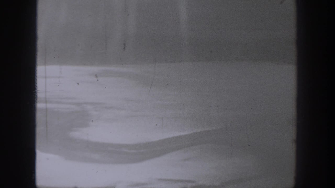 A 1940 Washington 8mm frame appears to look through dark bars at a bright blurred surface, with visible grain and wear.