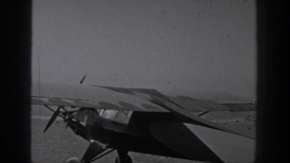 A small propeller aircraft appears on an open airfield surface in Washington, 1940, partly obscured by dark vertical bars.