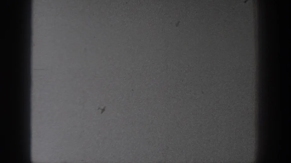 A mostly blank 8mm frame shows gray texture, dark side bars, dust marks, and scratches after the airplane shot.