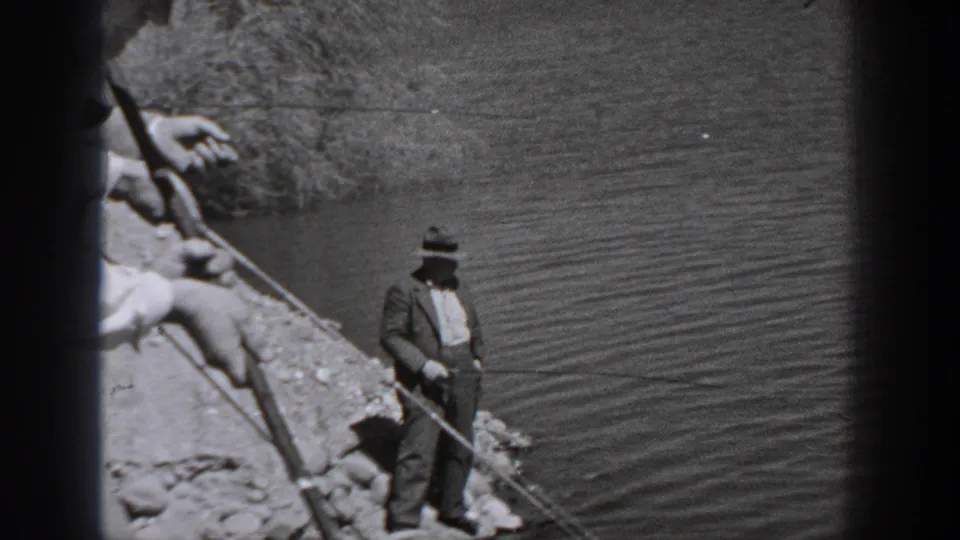 Washington riverside home-movie frame from 1940 showing a man fishing as another person handles a rod in the foreground.
