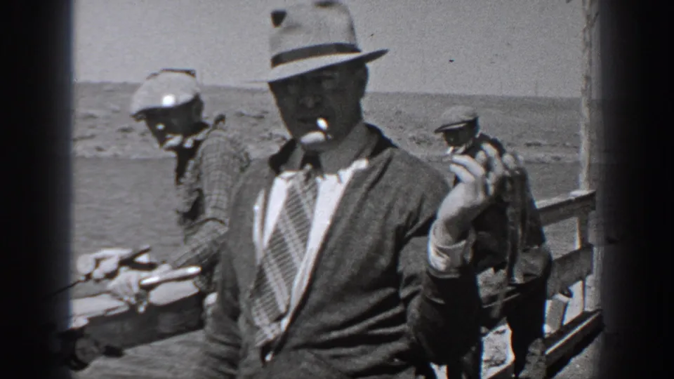 Washington 1940 home-movie frame showing men on a dock with fishing gear and one man in a fedora holding a pipe.