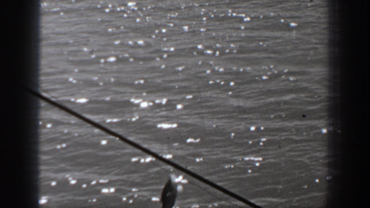 Fishing line stretches over bright rippling water with a small catch hanging near the frame edge.