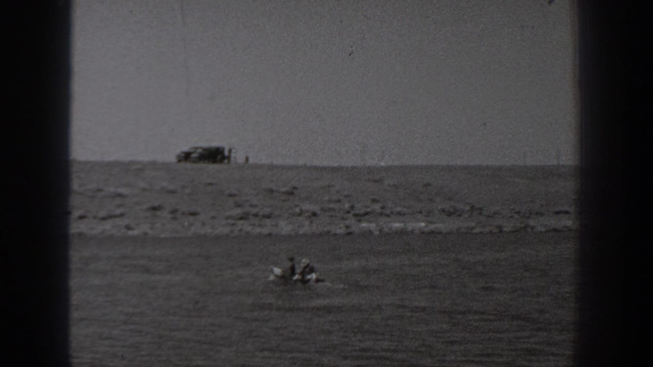Distant small boat on water with rocky shore and parked vehicle along the horizon.