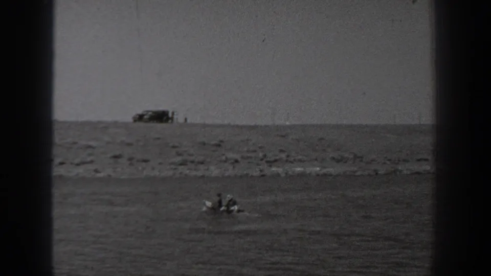 Black-and-white 8mm view from Washington in 1940, with a small boat on the water and a vehicle on the shoreline ridge.