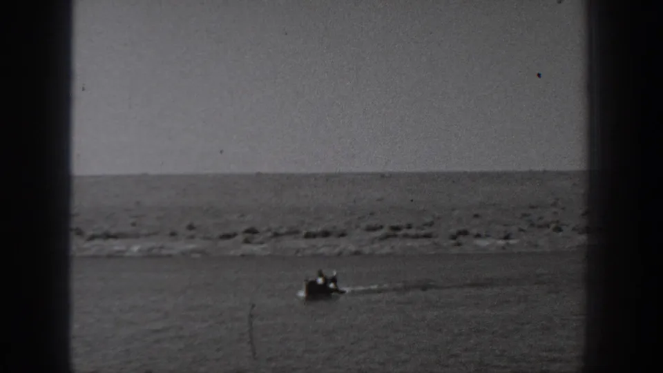 1940 Washington home-movie frame showing a distant boat on calm water with shoreline and sky beyond.