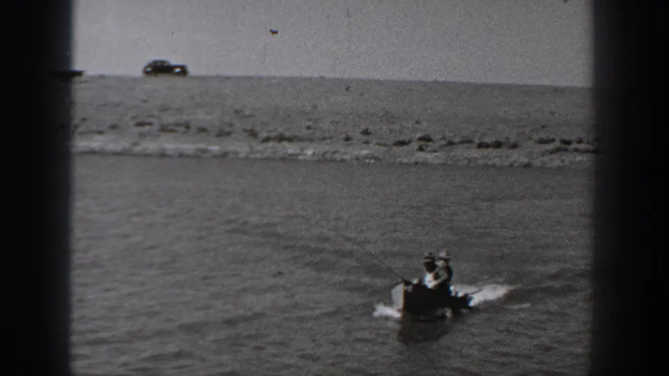 1940 Washington 8mm frame of people in a small boat on water, with a distant car on the shoreline.