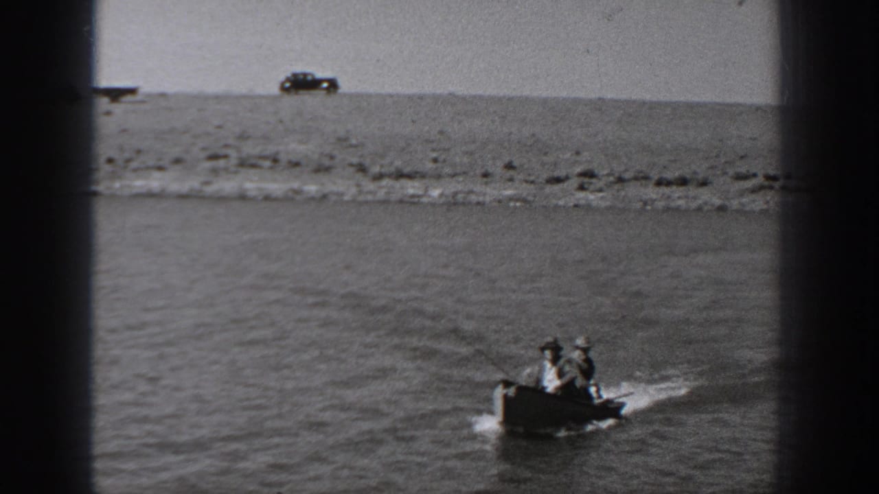 In 1940 Washington home-movie footage, two men ride a small motorboat on a river with a parked car visible on the far bank.