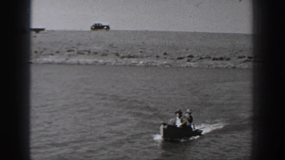 In 1940 Washington home-movie footage, two men ride a small motorboat on a river with a parked car visible on the far bank.
