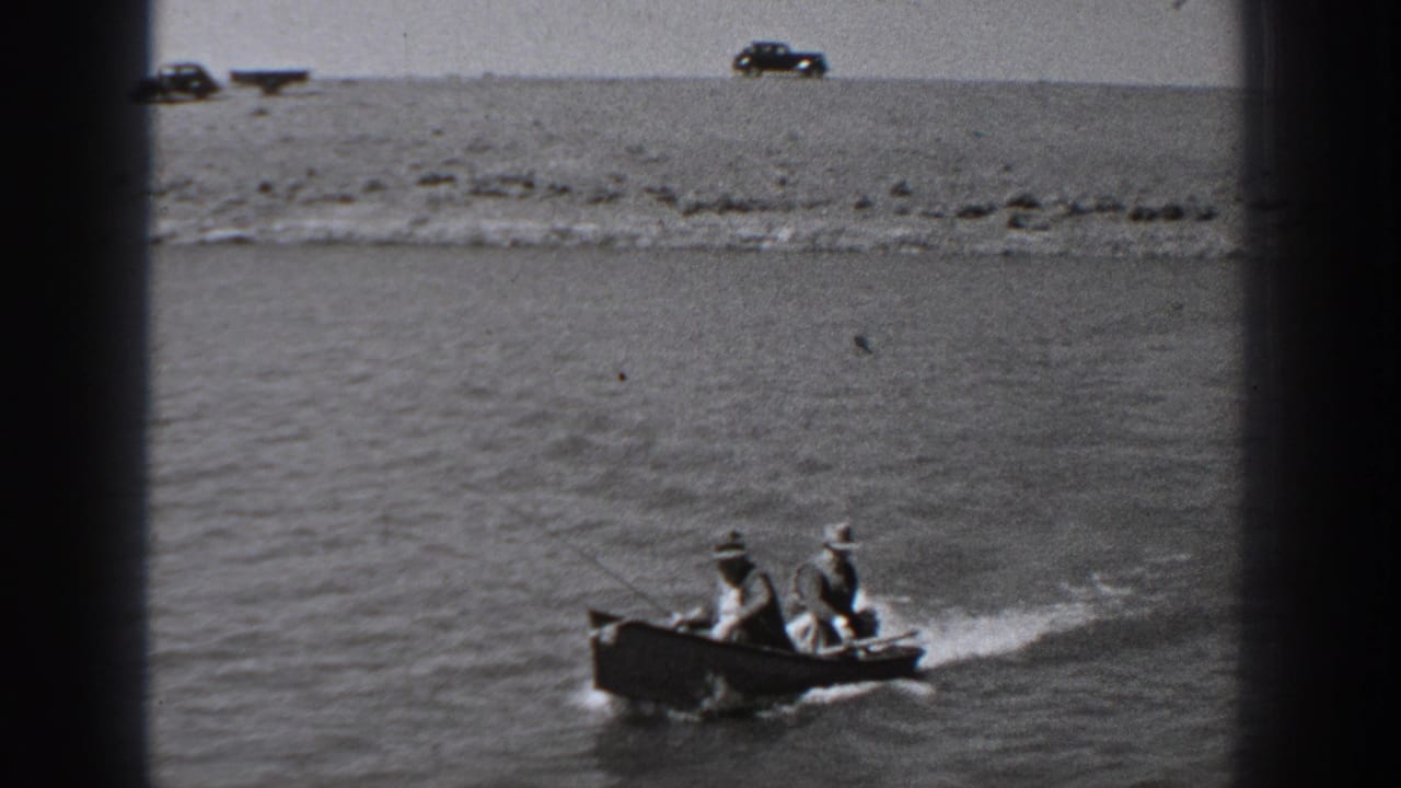 A small motorboat carrying two men creates a wake on open river water.