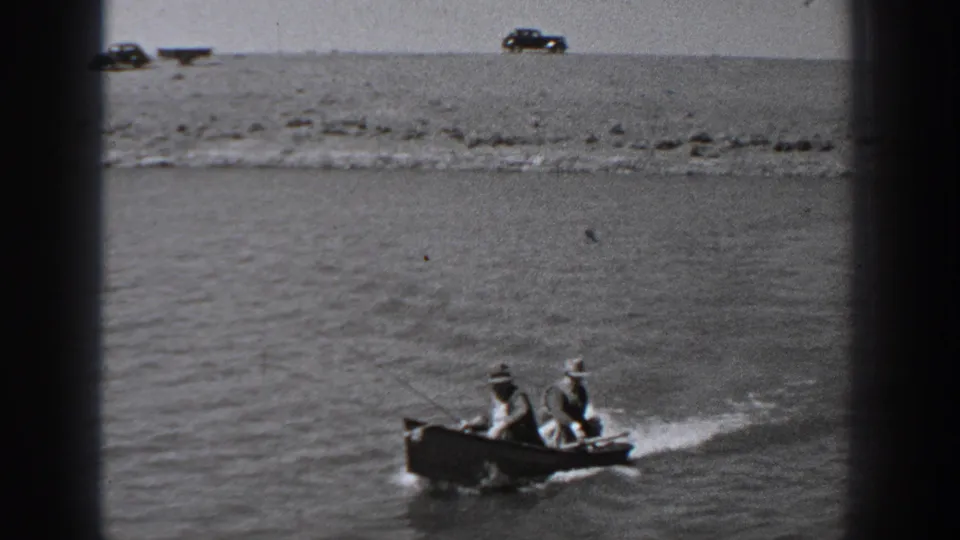 Two men in hats ride a small motorboat through a Washington river scene, leaving a pale wake below a rocky shoreline.