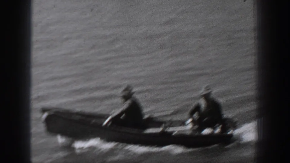 A closer, motion-blurred 1940 Washington frame shows two men in hats seated in a small motorboat as it crosses the water.