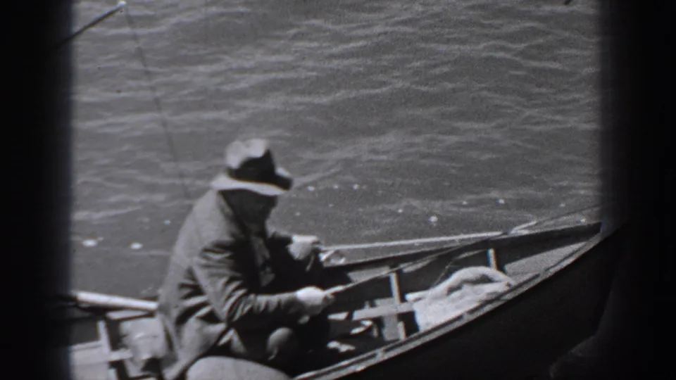 A seated man in a brimmed hat and coat holds a fishing rod in a small boat on Washington water in this 1940 home-movie frame.