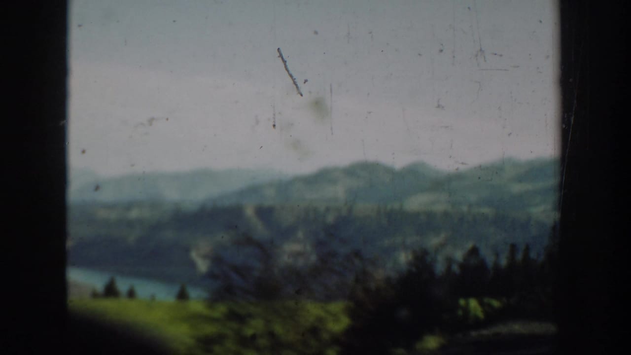 1940s Washington 8mm frame showing a river, rolling hills, distant mountains, and dark vehicle-window edges.