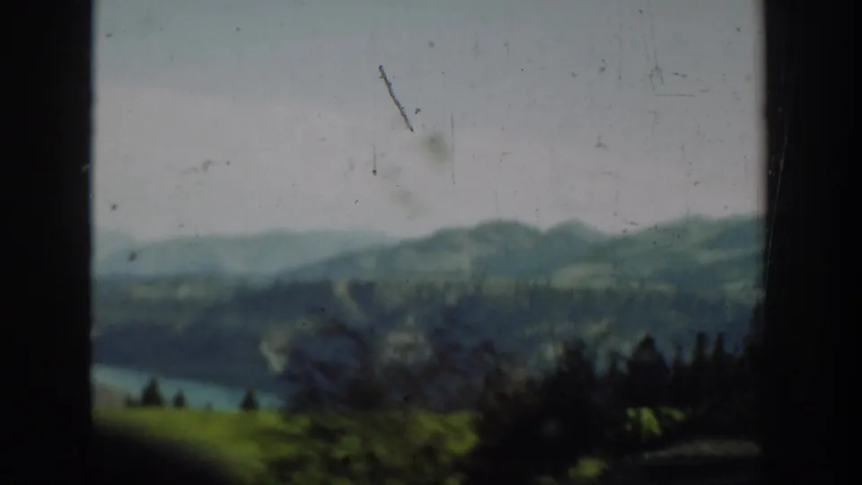 1940s Washington 8mm frame showing a river, rolling hills, distant mountains, and dark vehicle-window edges.