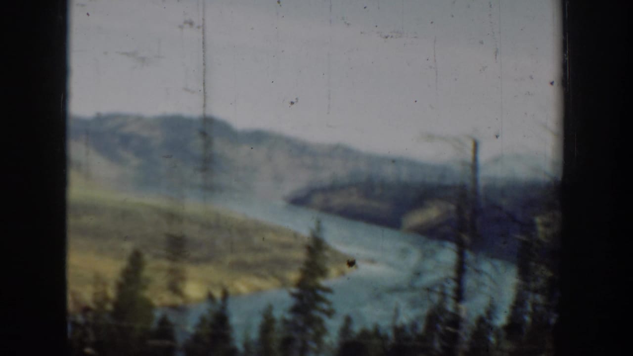 Winding river beside hills and evergreen trees, framed by a dark window edge.