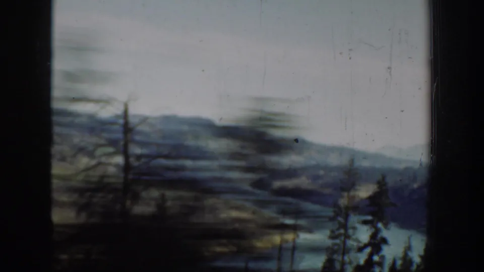 Motion-blurred 1940s Washington 8mm frame with roadside trees, river water, and distant hills passing the camera.