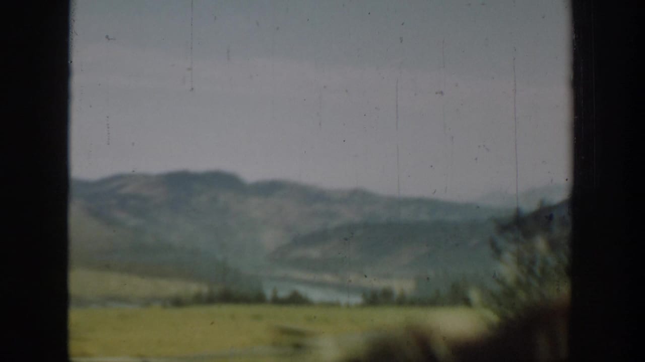 Blurred mountain valley and water beyond a dark vertical window divider.