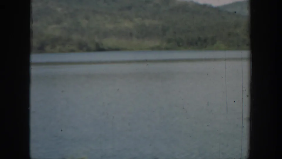 1940 Washington 8mm frame showing a calm lake below a wooded hillside, with dark vertical framing at the sides.
