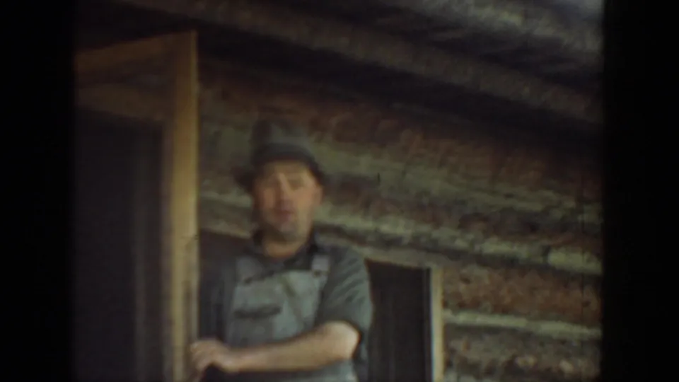 Adult man in a cap and work shirt stands in a log cabin doorway in Washington 1940 home-movie footage.