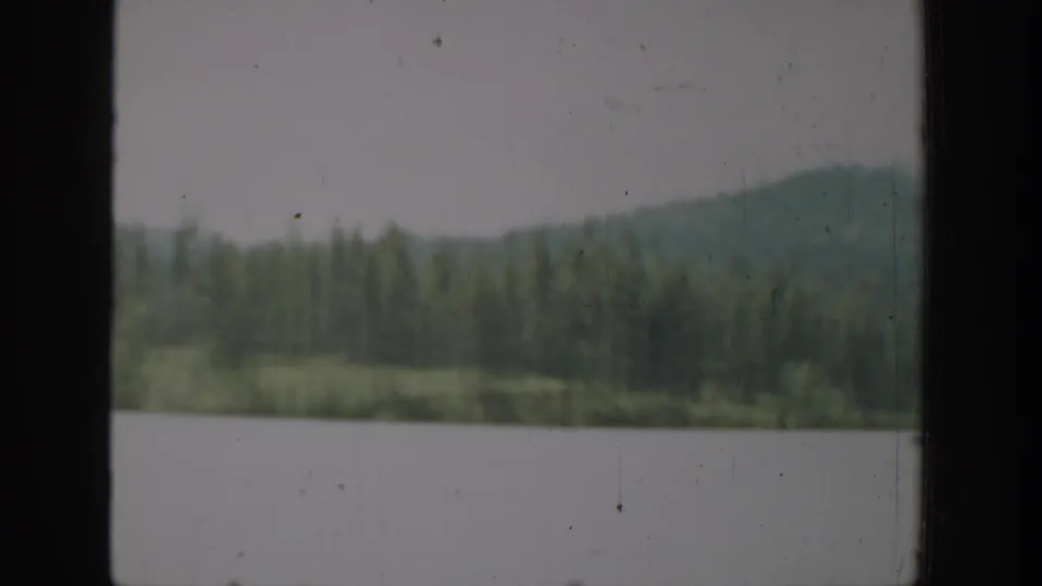Washington 1940 home-movie frame of a calm lake bordered by evergreens and low hills, with visible film wear.