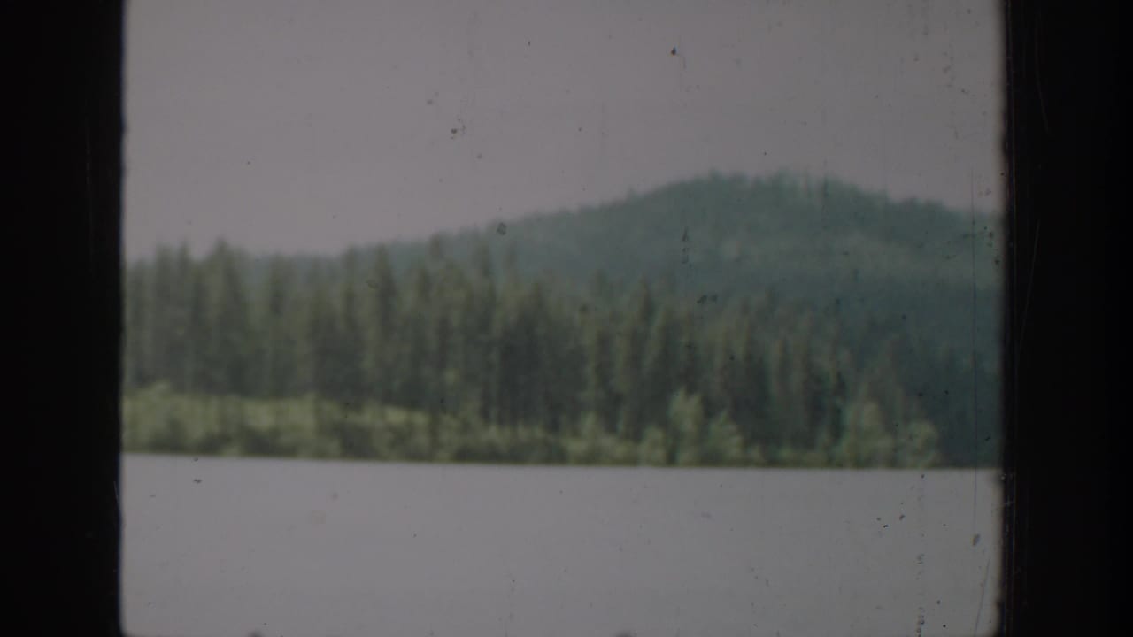 1940 Washington 8mm frame showing a lake and evergreen hillside through a vertical window frame, with soft focus and visible film wear.