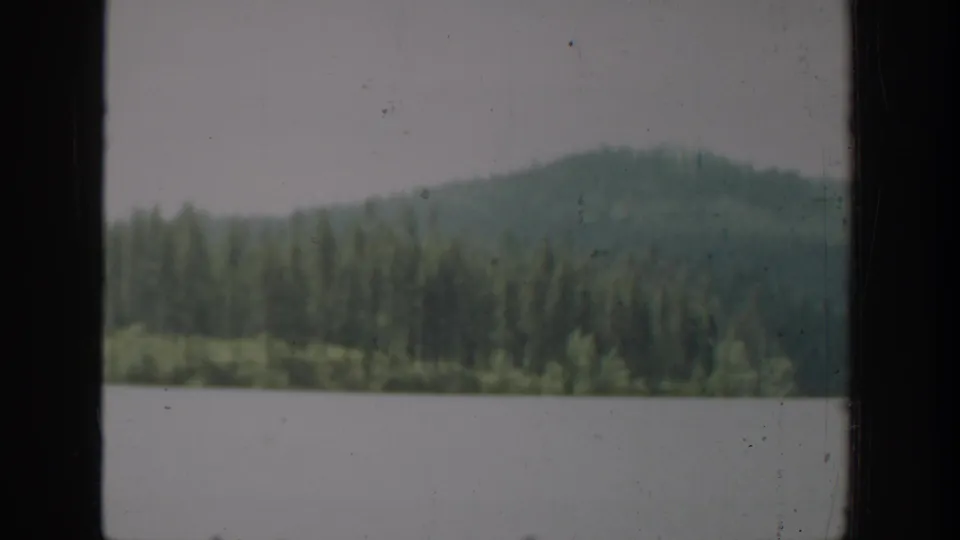 1940 Washington 8mm frame showing a lake and evergreen hillside through a vertical window frame, with soft focus and visible film wear.