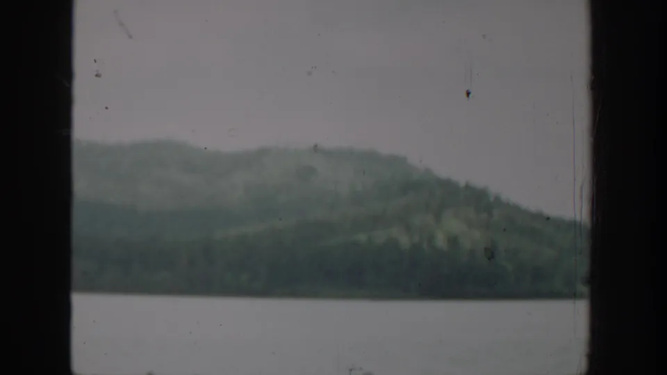 1940 Washington 8mm scenery with a calm lake, low forested hills, and a dark window frame at the left edge.