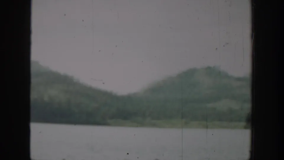 1940 Washington 8mm frame with rounded green hills across a lake, viewed through dark window framing and archival surface marks.