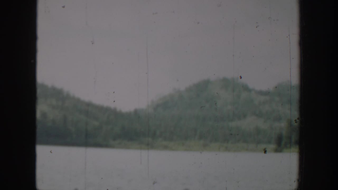 Lake and forested hills viewed through dark vertical framing.