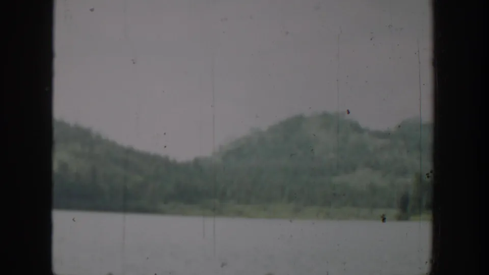 1940 Washington 8mm frame showing a lake, evergreen shoreline, and hazy hills seen through a dark opening.