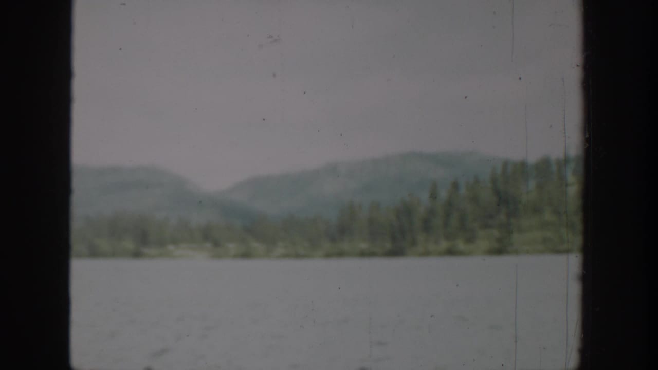 Wide lake with distant forested hills under an overcast sky.