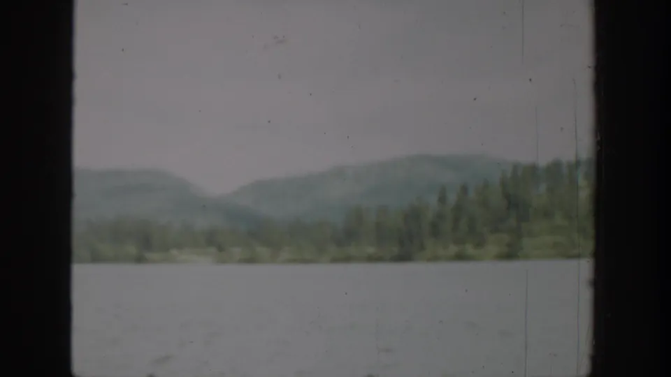 1940 Washington 8mm view across a broad lake toward evergreen-covered hills and hazy mountain slopes.