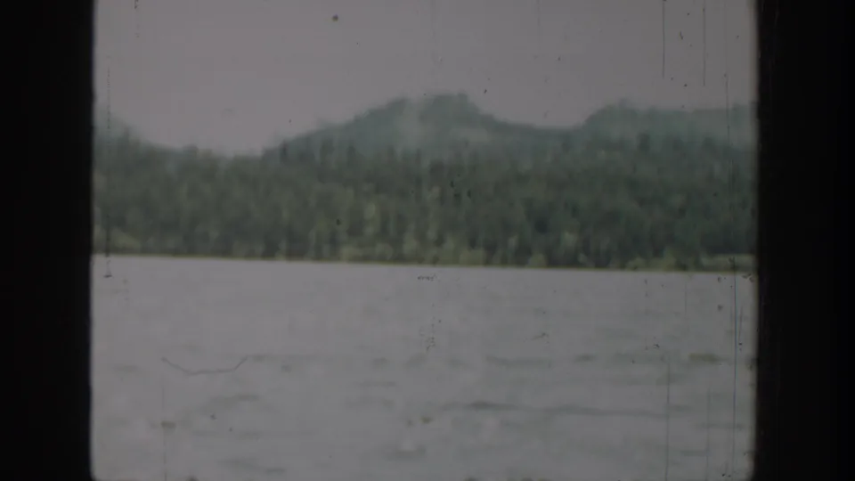 1940 Washington 8mm frame showing choppy lake water below evergreen hills, with dust and scratches visible on the film.
