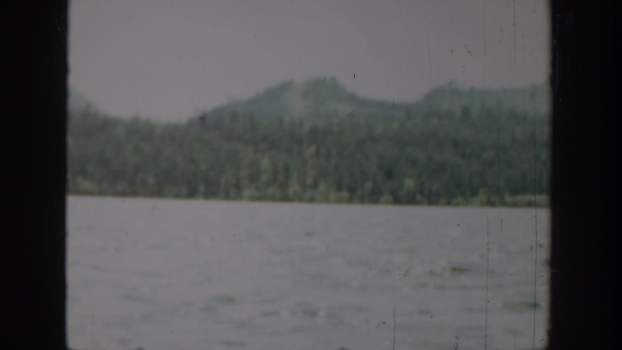 1940 Washington 8mm view of rippled water, forested hills, and soft mountains seen through a dark frame edge.